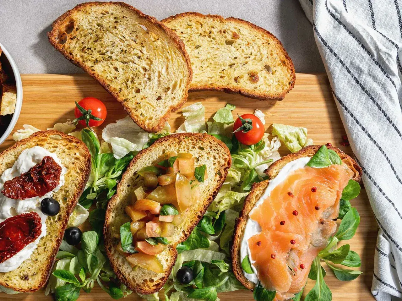 Bruschette senza pomodoro: fette di pane tostato con salmone, crema, pomodori secchi e verdure fresche.
