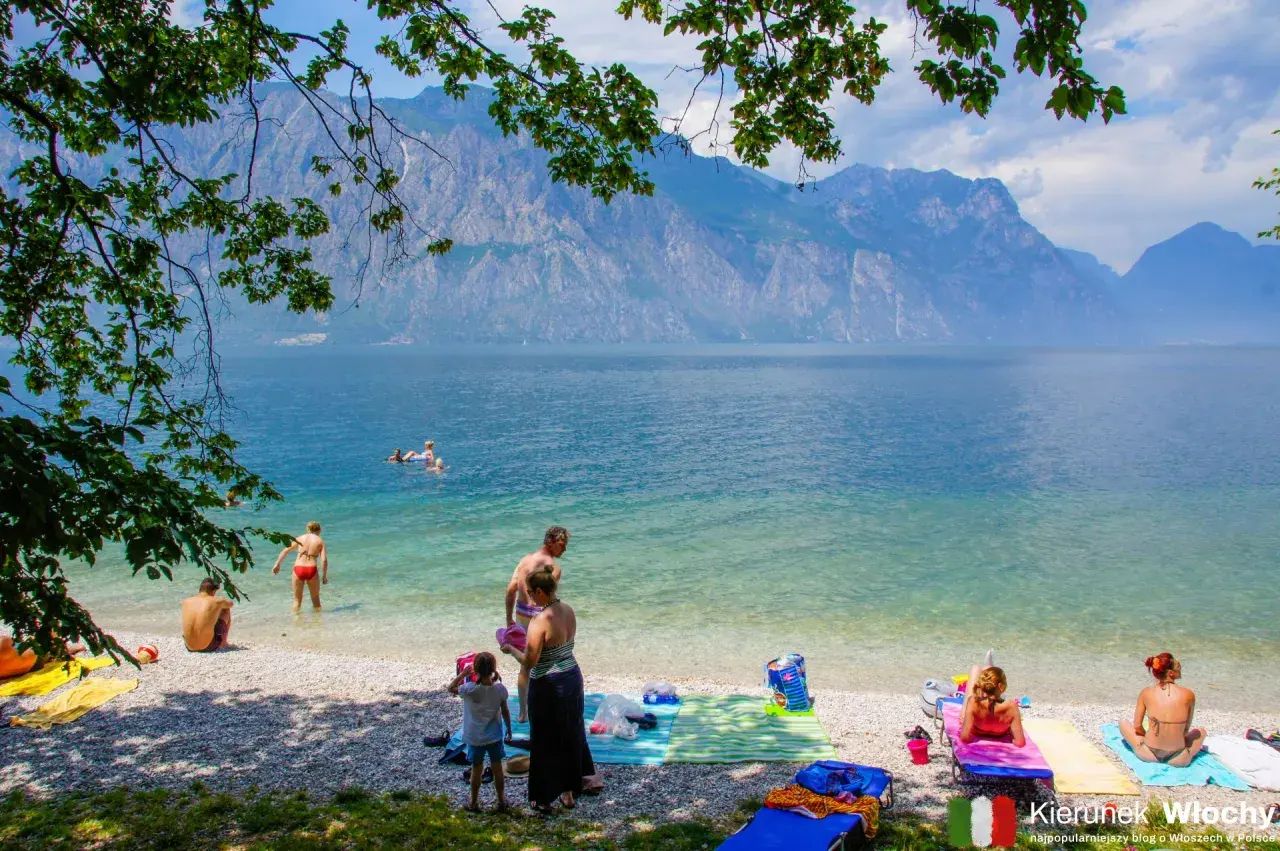 Ludzie odpoczywają na żwirowych plażach nad Jeziorem Garda, podziwiając góry.