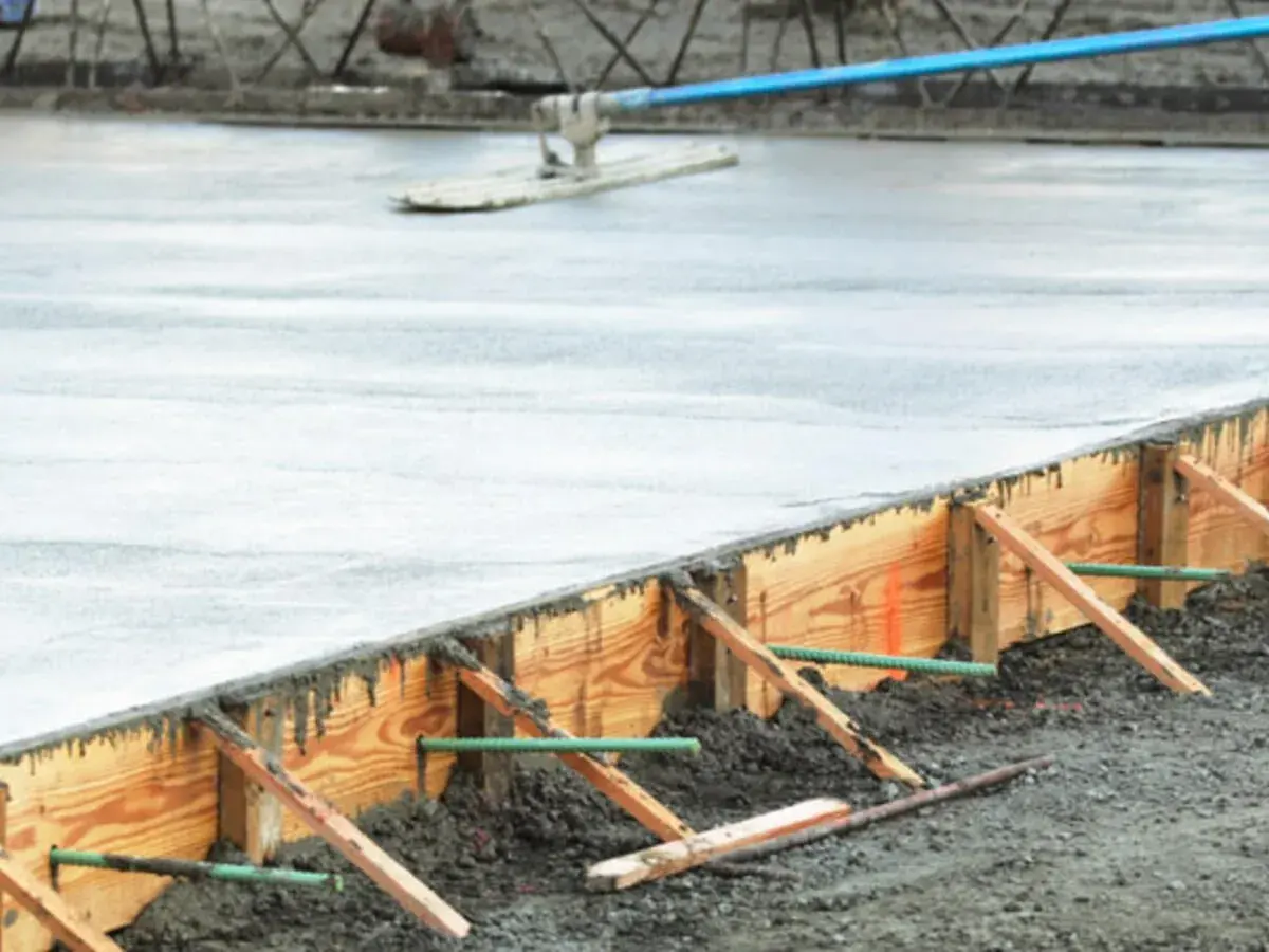 Frisch gegossener Beton wird mit einem Abzieher geglättet. Die verlorene Schalung aus Holz hält den Beton in Form, während er aushärtet.