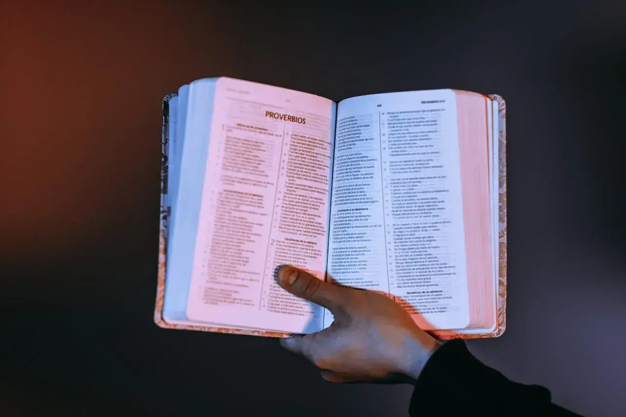 Otwarta księga z tekstem, dłoń przytrzymująca strony. Czy testament bez notariusza jest ważny? Warto szukać odpowiedzi w mądrych księgach.