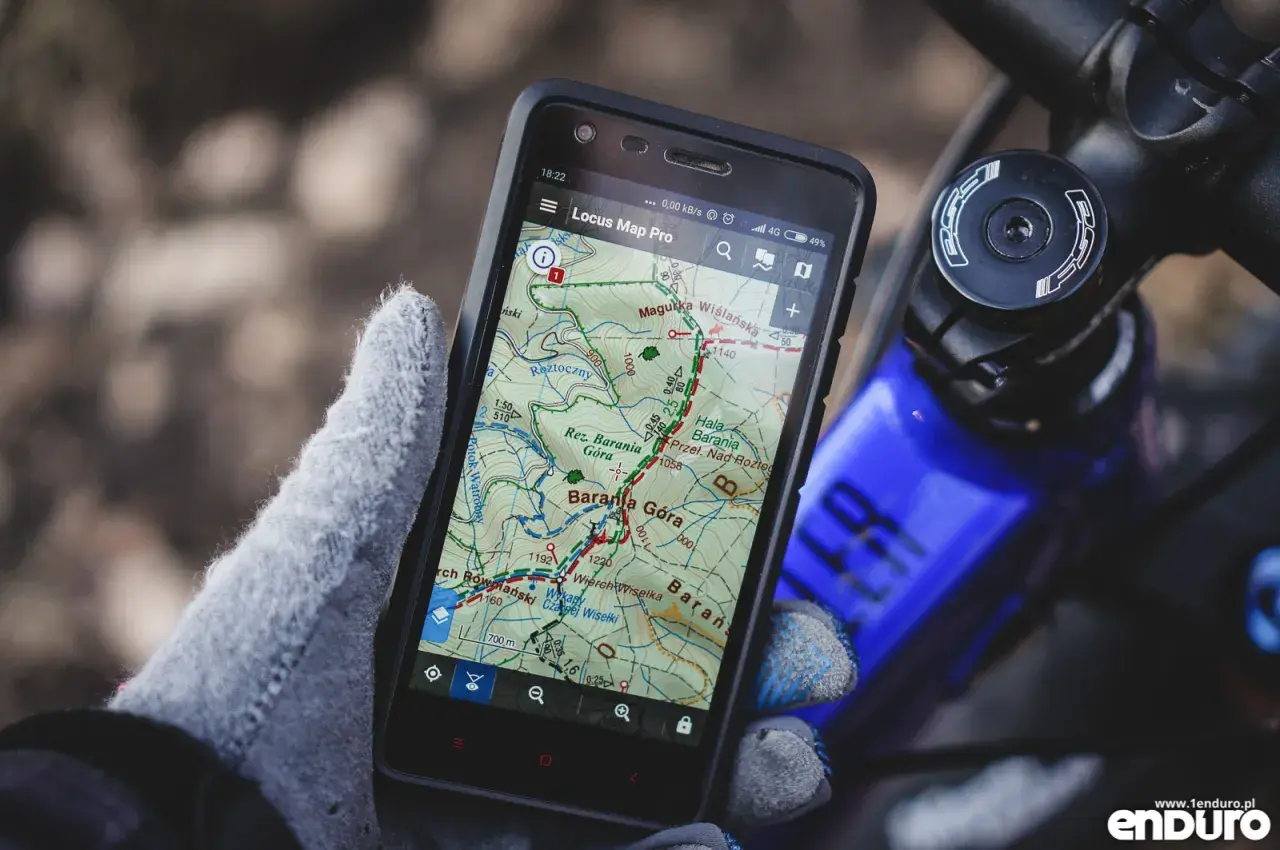 Rękawica trzyma smartfon z aplikacją szlaki turystyczne Locus Map Pro, pokazującą trasę w górach.