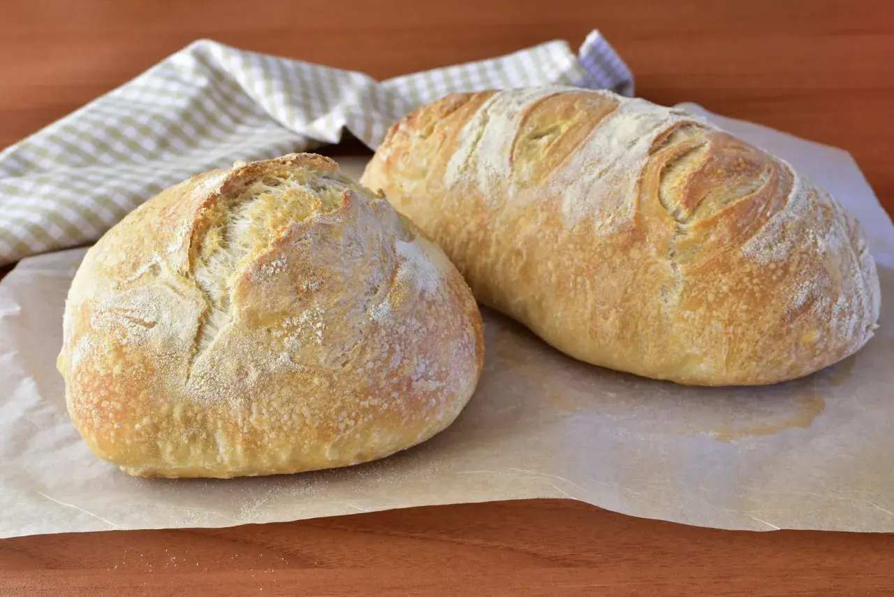 Due pagnotte di pane morbido fatto in casa, dorate e leggermente infarinate, su carta da forno.