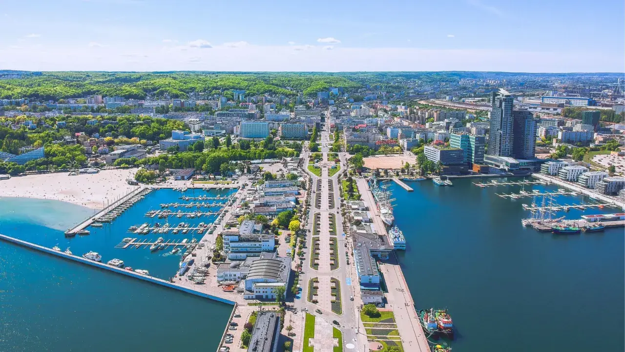 Gdynia o wszystkim: port jachtowy, plaża, nowoczesne budynki i zielone wzgórza. Widok z lotu ptaka na tętniące życiem miasto nad Bałtykiem.