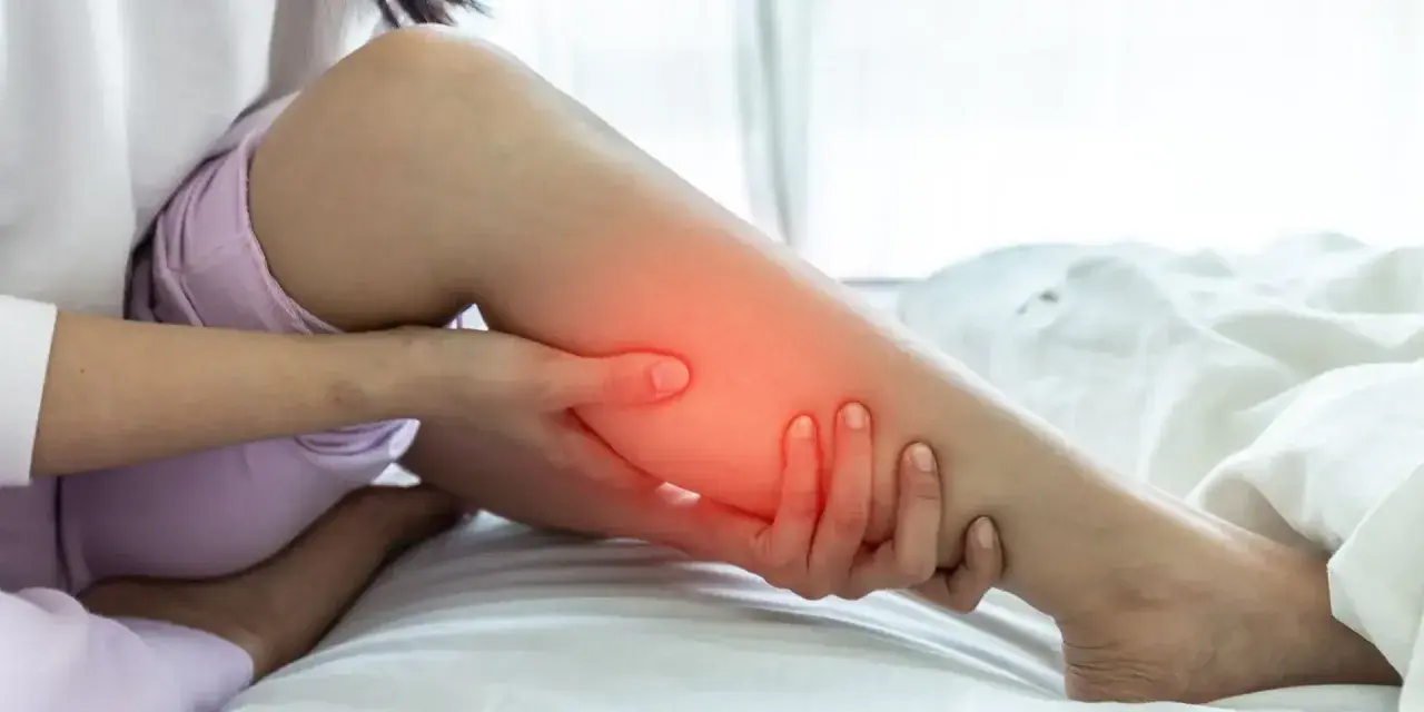 Une personne se tient la jambe, une zone rouge vif sur le mollet indiquant une douleur.