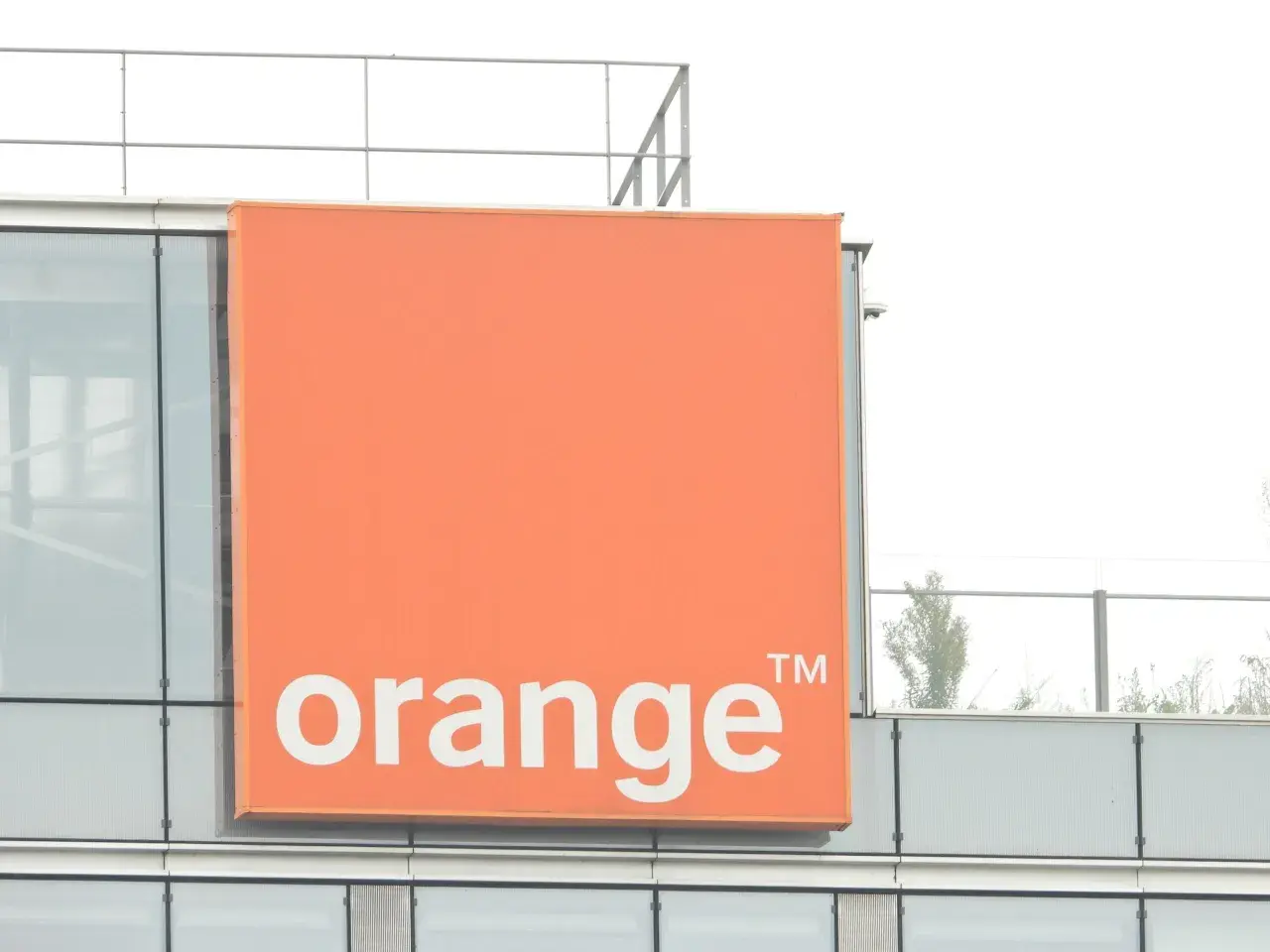 Pomarańczowy znak z napisem "orange" na nowoczesnym budynku. To logo firmy telekomunikacyjnej, która oferuje usługi multiroom.