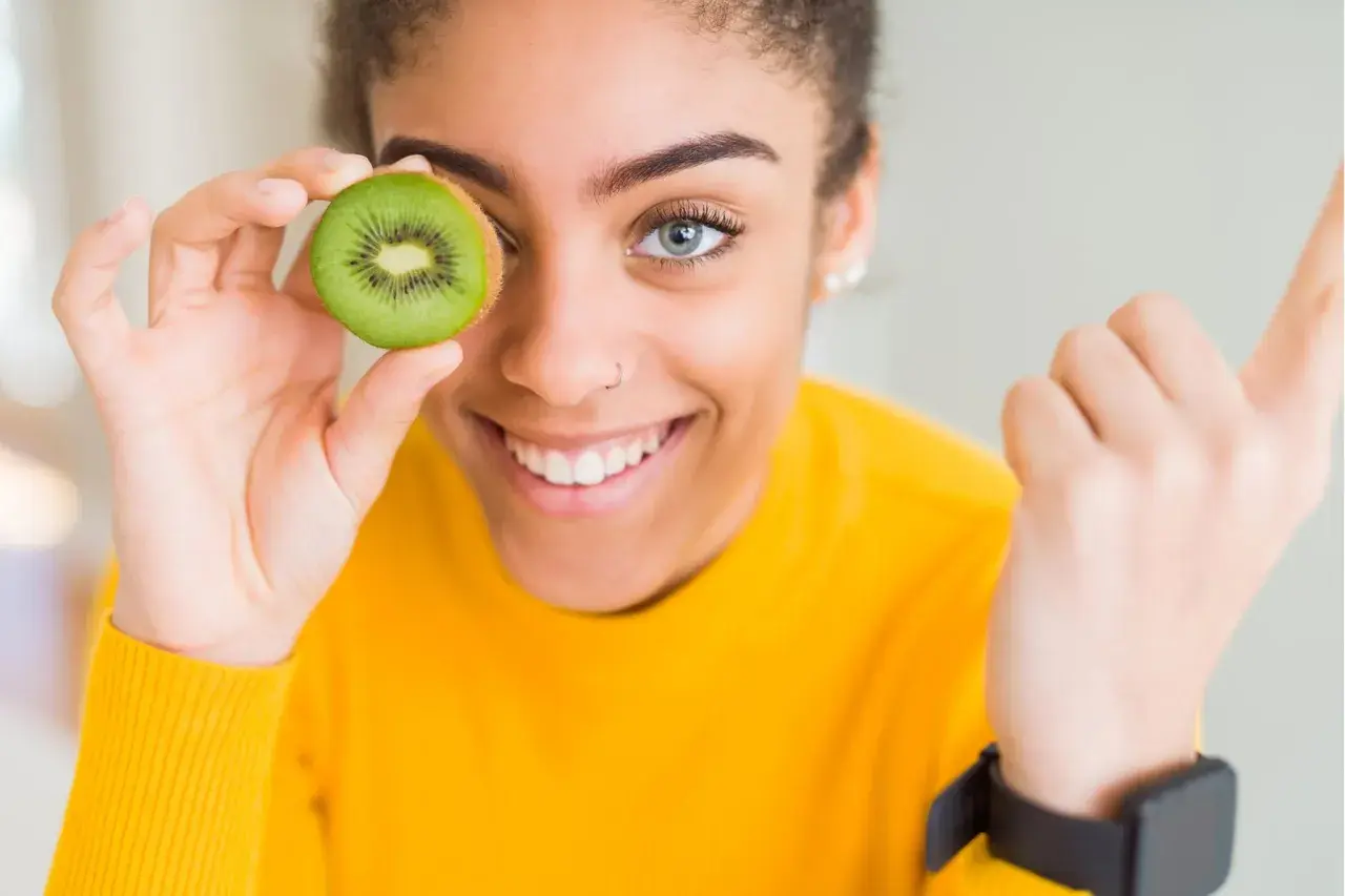 Junge Frau hält Kiwi vor ihr Auge, ein Symbol für gesunde Ernährung und eine gesunde Leber.