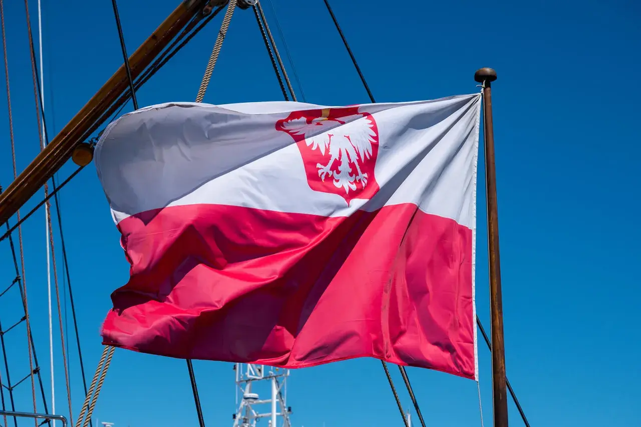 Flaga bandery w Polsce, biało-czerwona z orłem, powiewa na maszcie żaglowca na tle błękitnego nieba.