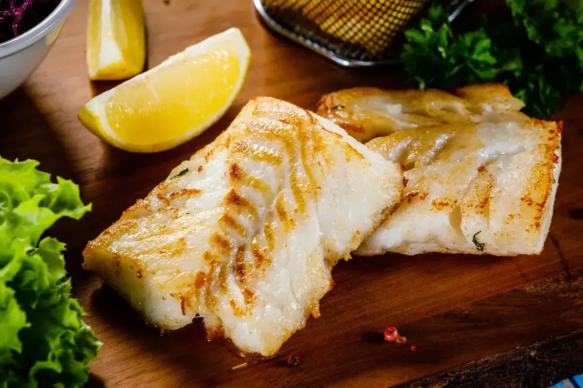 Filetti di branzino in padella in bianco, dorati e succulenti, serviti con spicchi di limone fresco e insalata croccante.