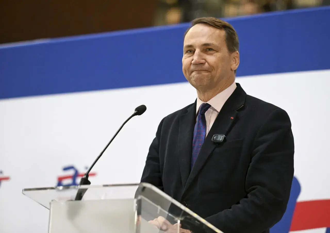 Mężczyzna w garniturze, podobny do Jana Sikorskiego, ojca Radosława Sikorskiego, przemawia przy mównicy.