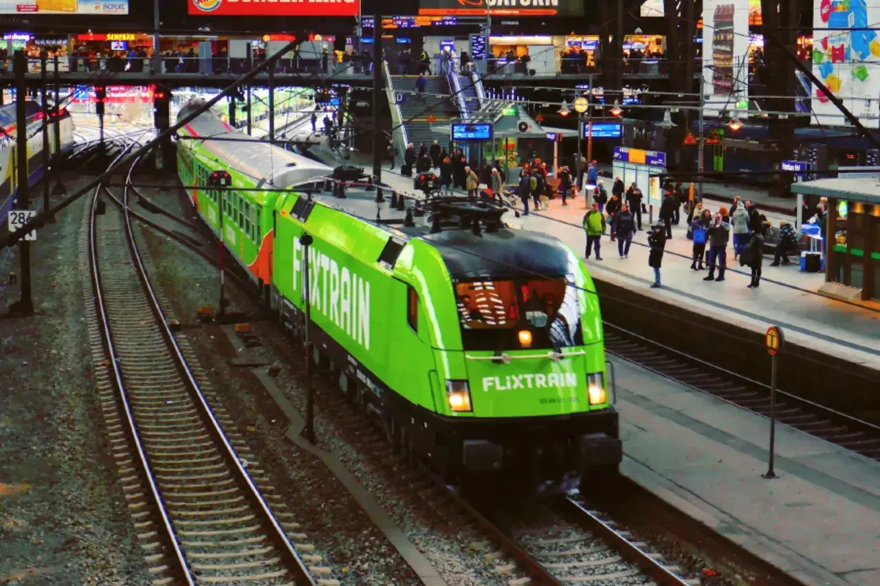 Ein grüner FlixTrain fährt in Berlin Hbf ein. Reisende warten auf dem Bahnsteig.
