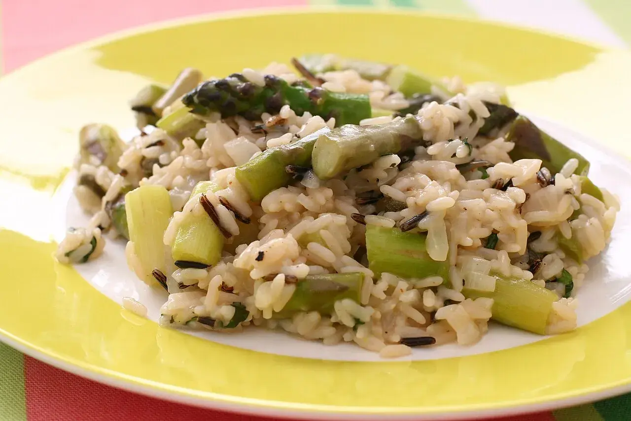 Pyszne risotto ze szparagami, z dodatkiem dzikiego ryżu, na żółtym talerzu.
