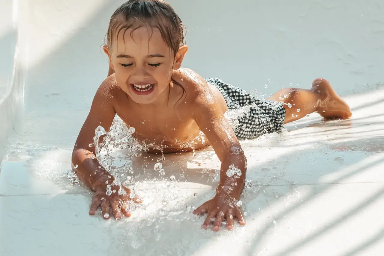 Enfant riant sur un toboggan aquatique, éclaboussures d'eau. Attention aux otites du baigneur symptômes après ces jeux !