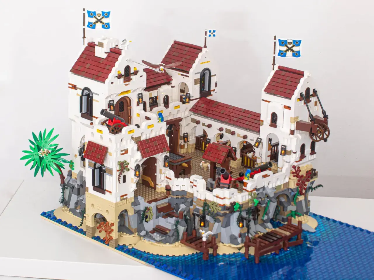 Eine beeindruckende Festung aus moc klemmbausteine, mit Kanonen, Flaggen und einem Steg am blauen Meer.