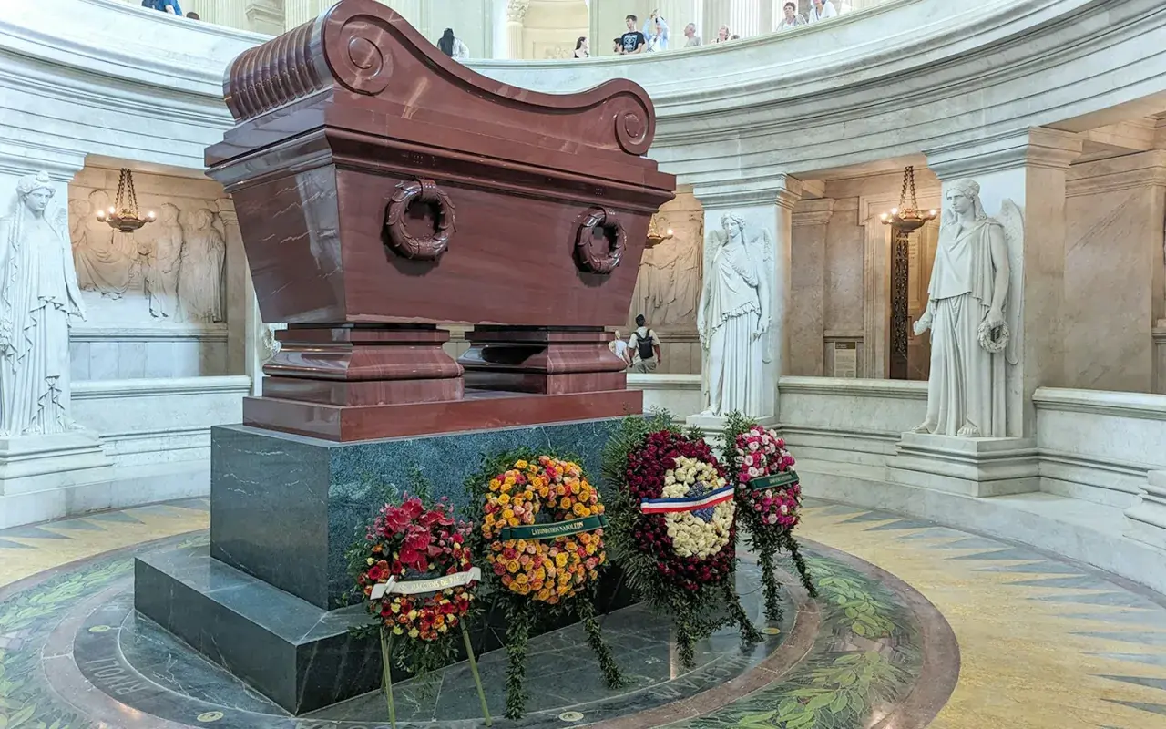 Imponujący sarkofag Napoleona, otoczony rzeźbami i wieńcami, w monumentalnym wnętrzu.