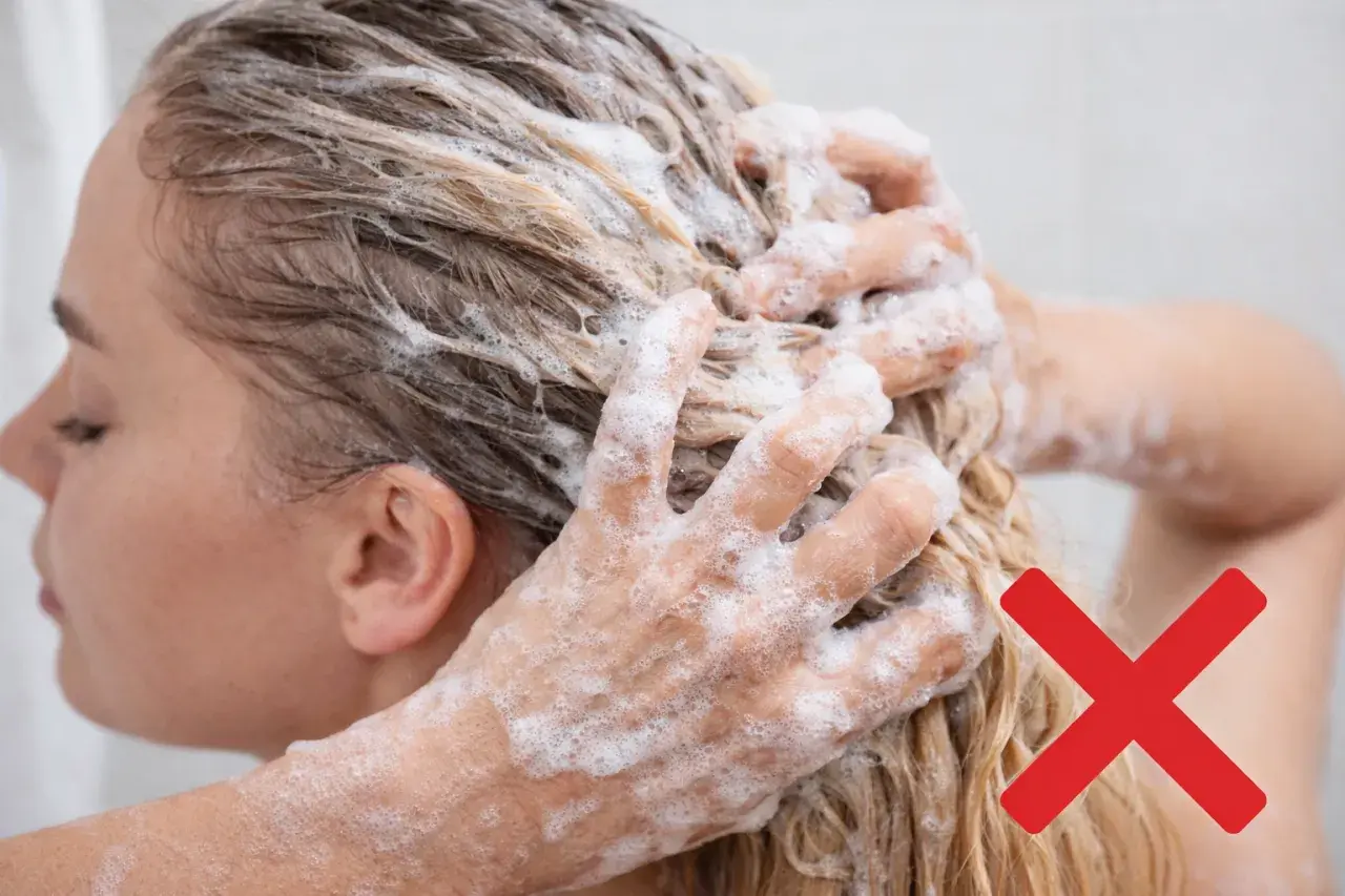 Mani che massaggiano shampoo sui capelli biondi, con una croce rossa che indica di evitare certi rimedi capelli grassi.