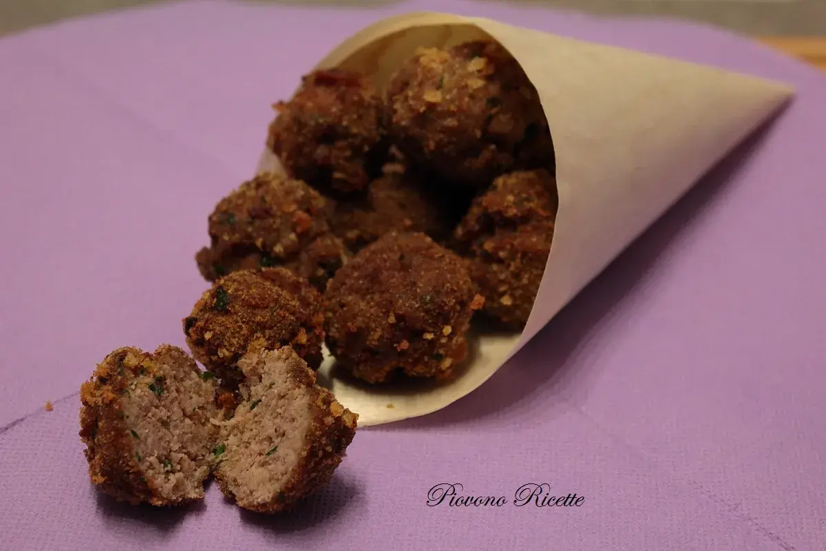 Un cono di carta pieno di polpette fritte dorate, una tagliata a metà rivela un interno succoso.