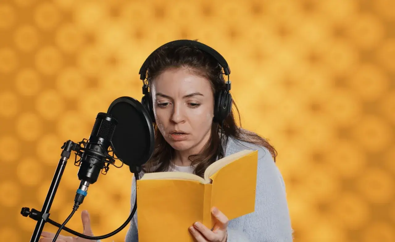 Eine Synchronsprecherin mit Kopfhörern liest ein Buch vor Mikrofon. Sie fragt sich, wie hoch wohl ihr Synchronsprecher Gehalt sein wird.