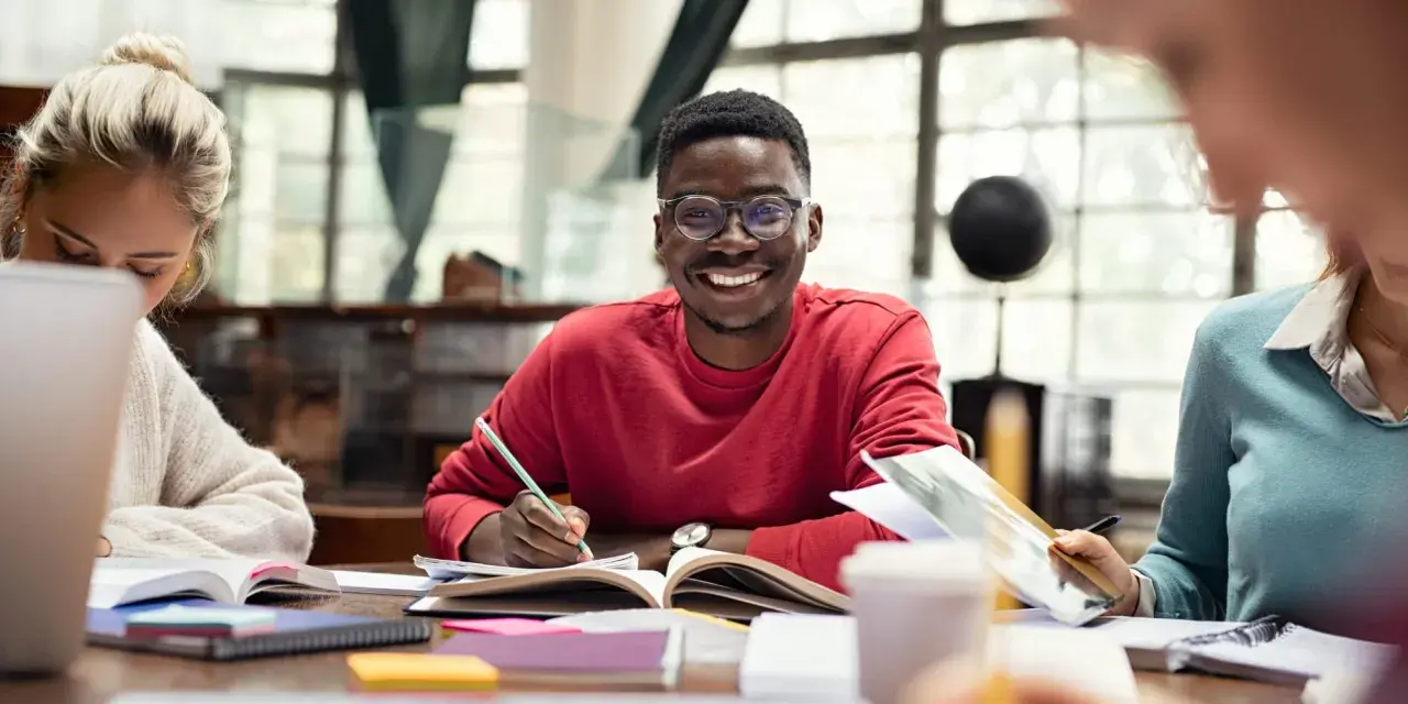 Jóvenes sonrientes estudiando juntos, una experiencia que inspira a estudiar en el extranjero.