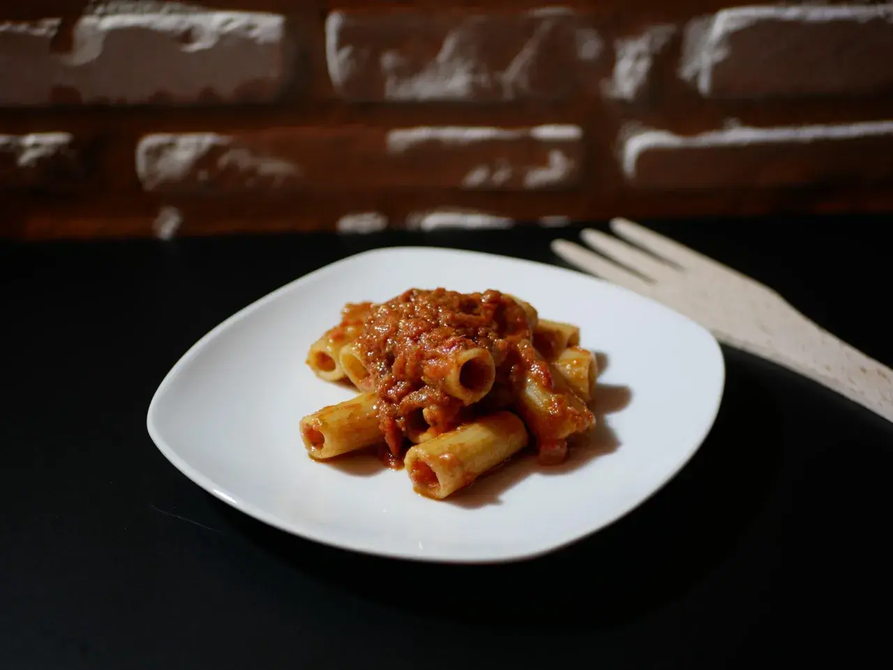 Piatto di pasta alla portofino con sugo rosso e forchetta in legno sullo sfondo di mattoni.