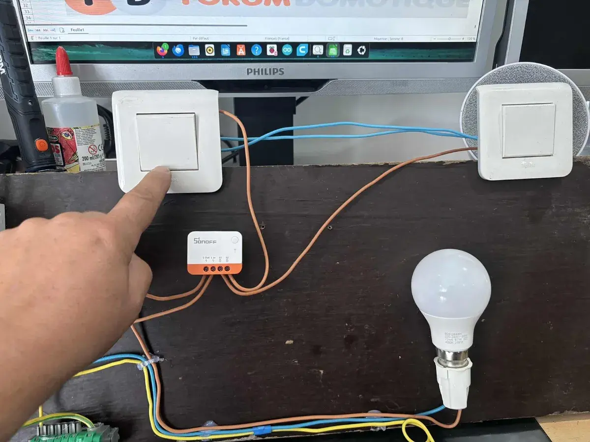 Installation d'un interrupteur zigbee va et vient. Un doigt actionne un interrupteur connecté à un module Sonoff, pilotant une ampoule.