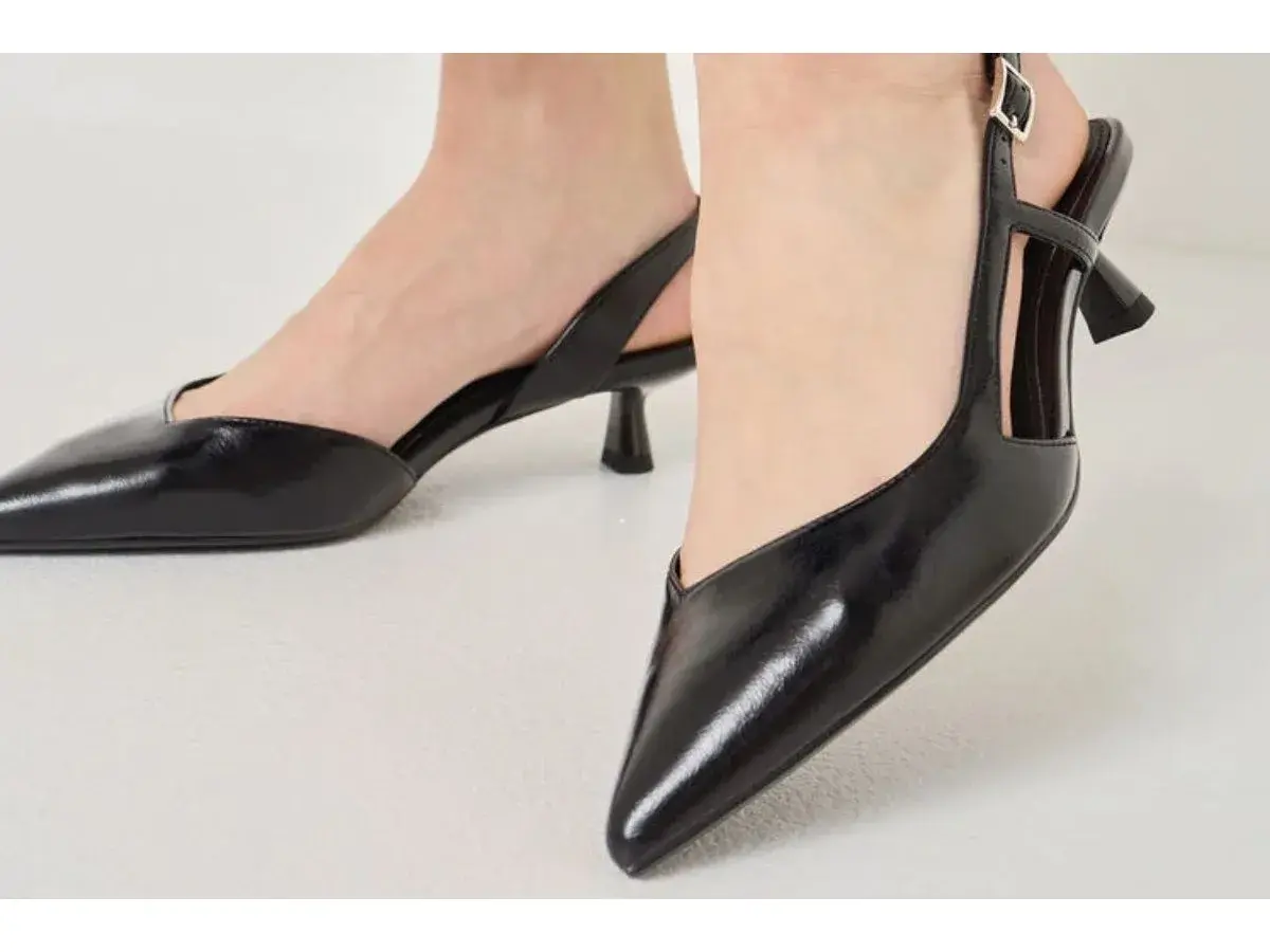 Pieds chaussés d'escarpins noirs vernis à talon carré et bride arrière. Idéal pour savoir comment porter des escarpins avec élégance.