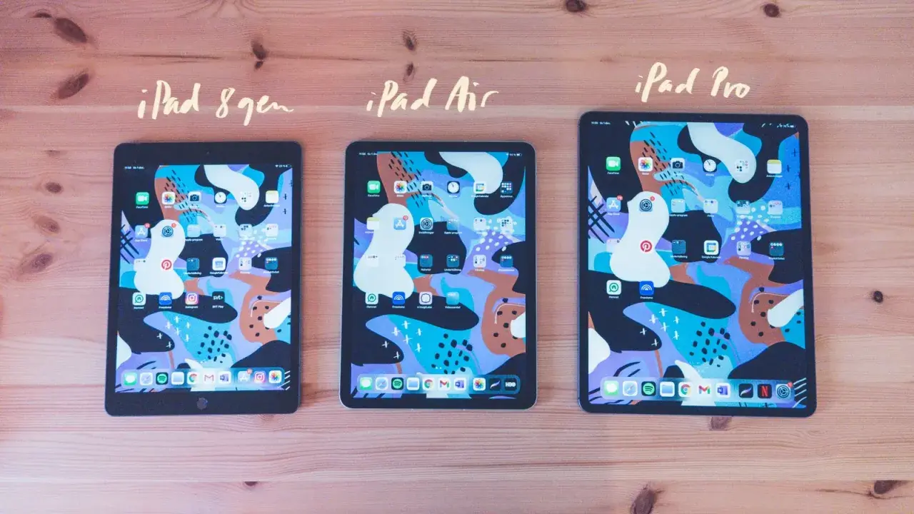 Tre iPads, 8:e gen, Air och Pro, ligger på ett träbord. Alla har samma färgglada bakgrundsbild och appar. Det är lätt att skriva på iPad.