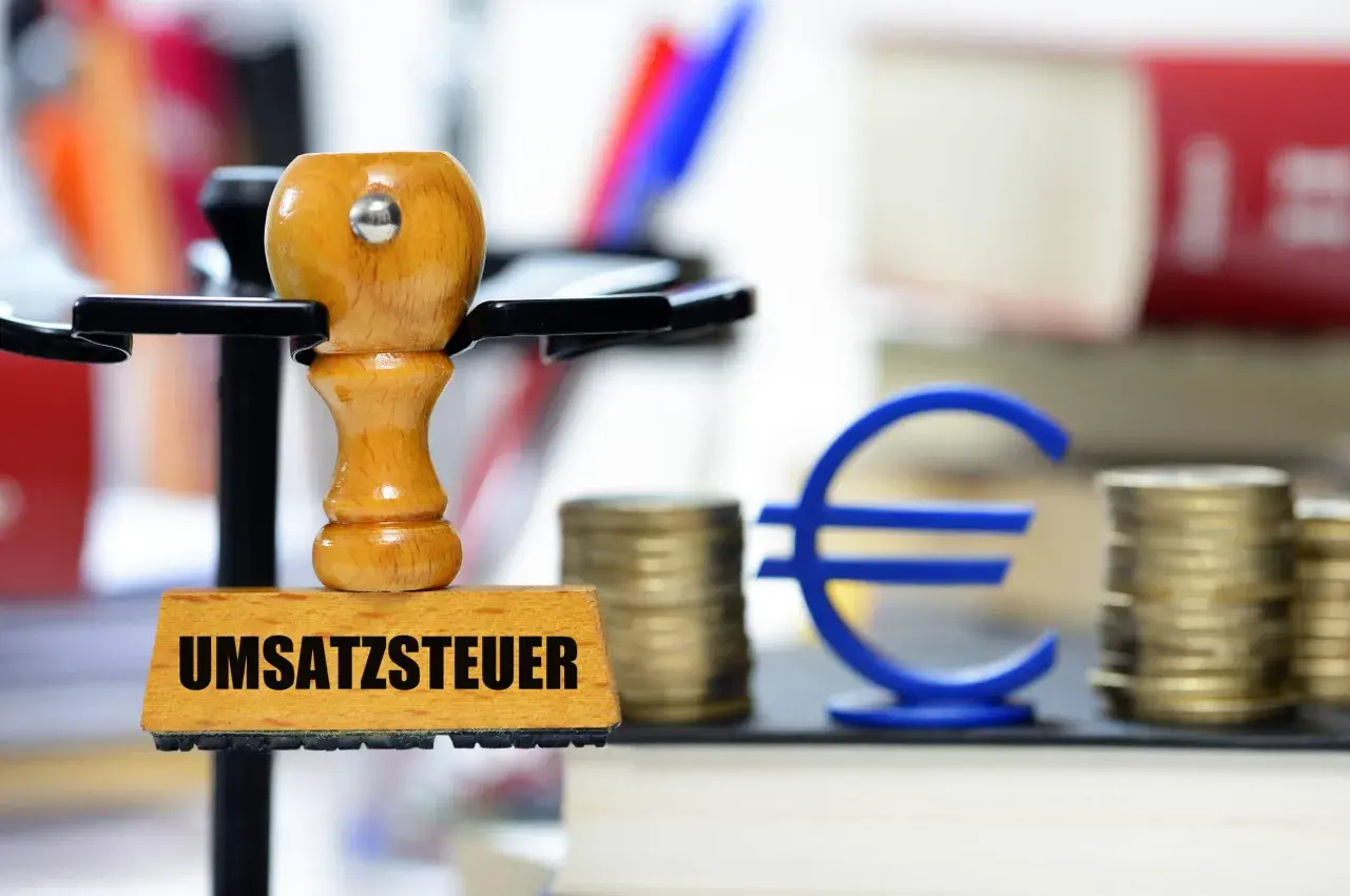 Stempel mit "Umsatzsteuer" und Euro-Symbol, Münzstapel und Bücher. Symbolisiert die regelbesteuerung landwirtschaft.