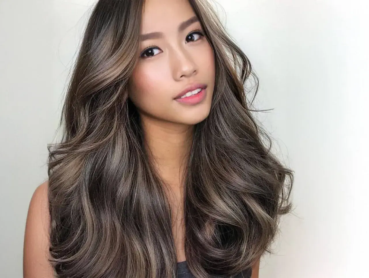 Mujer con cabello castaño con reflejos claros, ondulado y brillante. Descubre cómo dar brillo al pelo teñido para un look radiante.