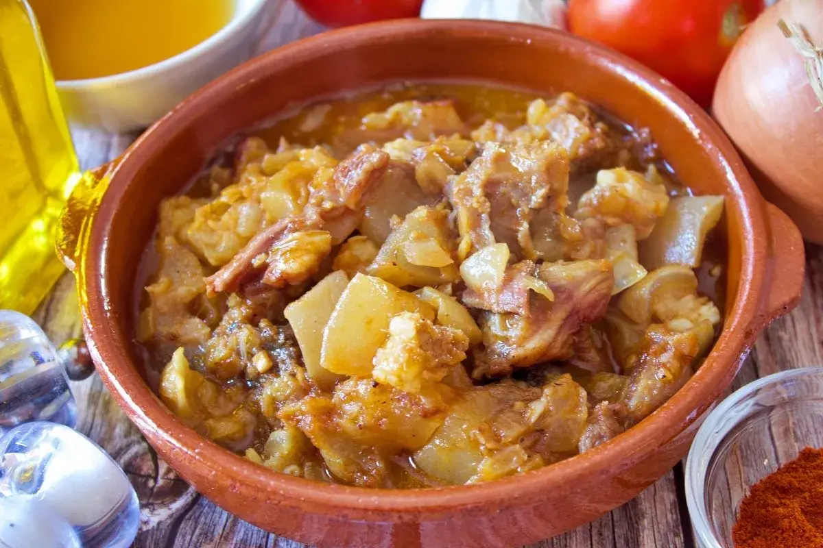 Guiso de cap i pota en cazuela de barro, con patatas y trozos de carne, acompañado de ingredientes frescos.