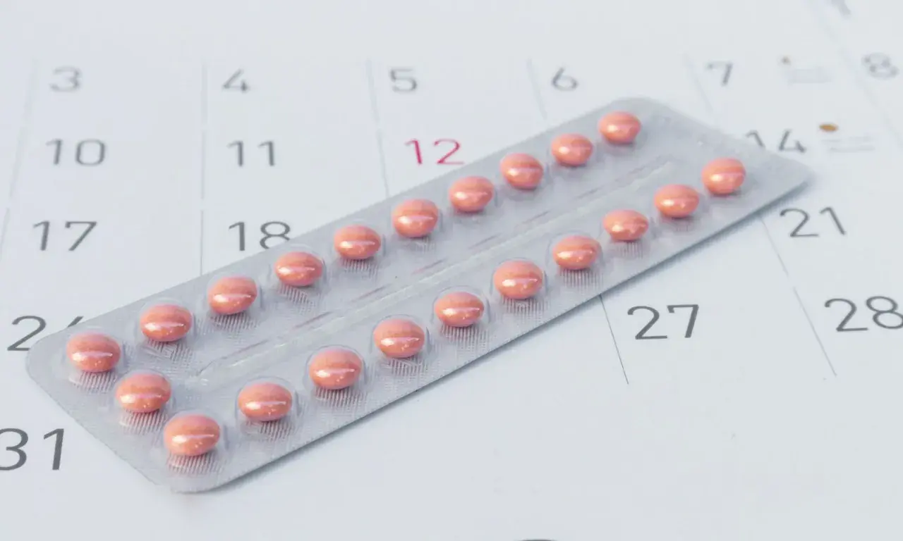 Blister z różowymi tabletkami antykoncepcyjnymi leży na kalendarzu, symbolizując różne rodzaje tabletek antykoncepcyjnych i planowanie.