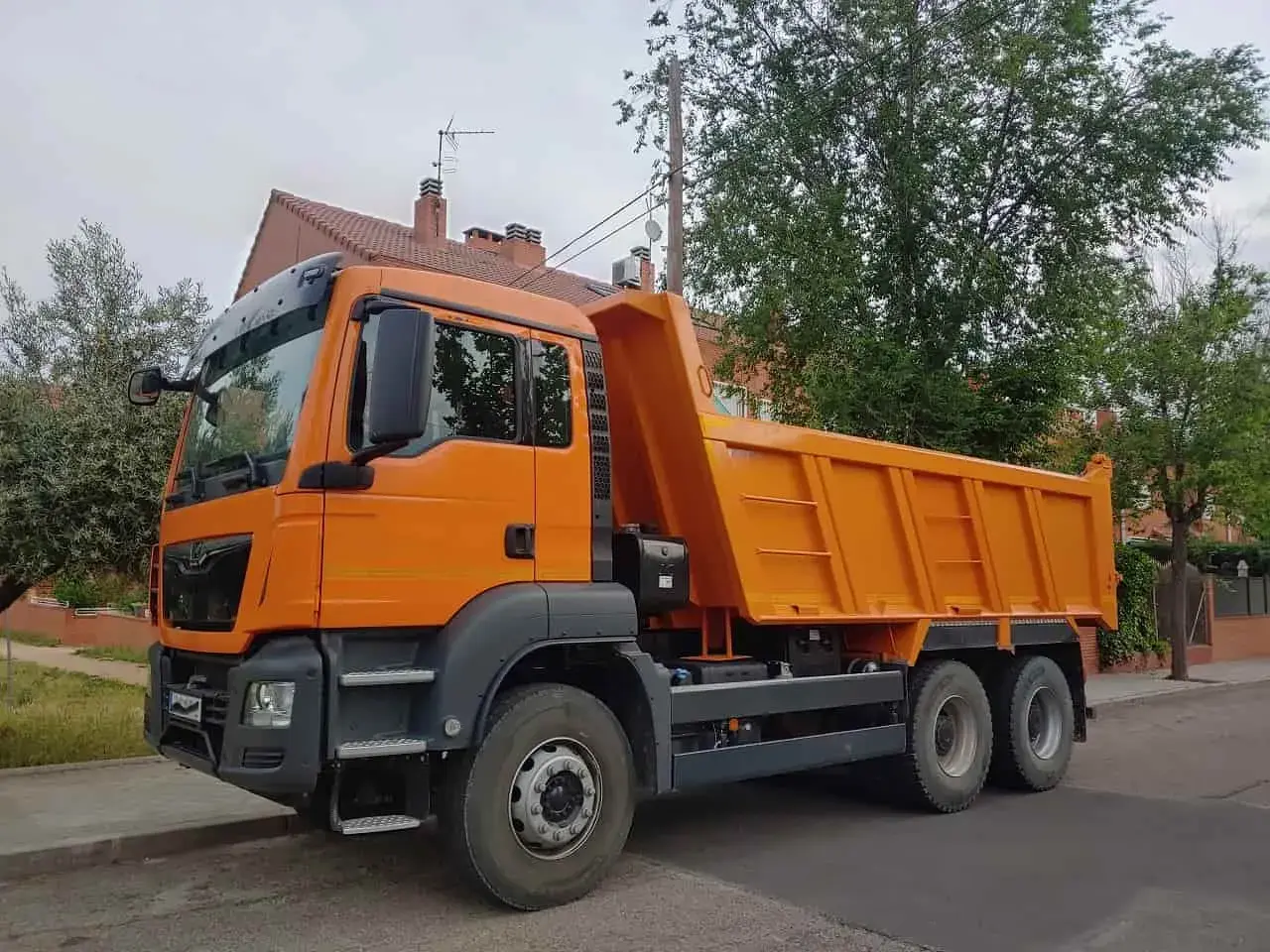 Pomarańczowa wywrotka, idealna do transportu materiałów budowlanych. Z kategorią C można ciągnąć taką przyczepę.