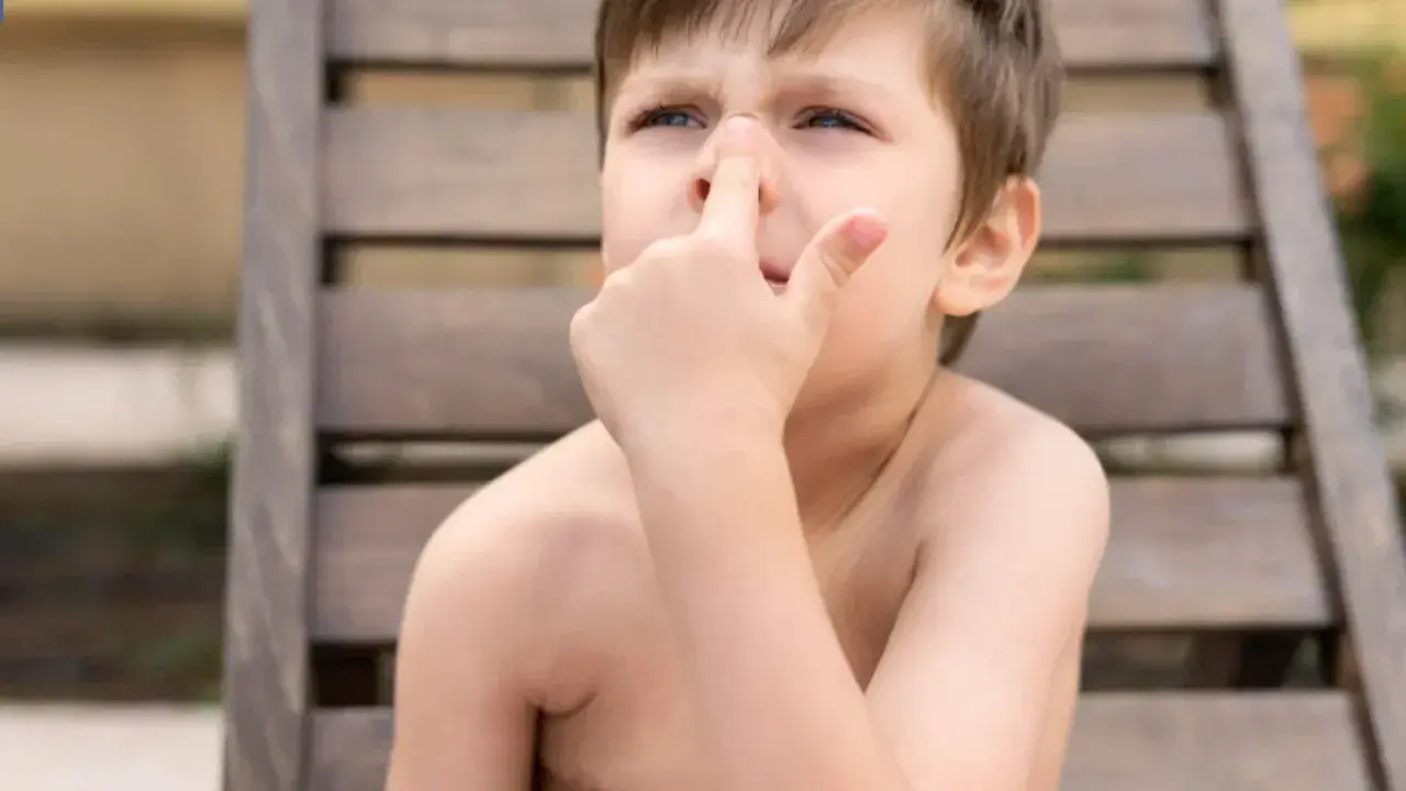 Niño con dedo en la nariz, quizás pensando en comerse los mocos.