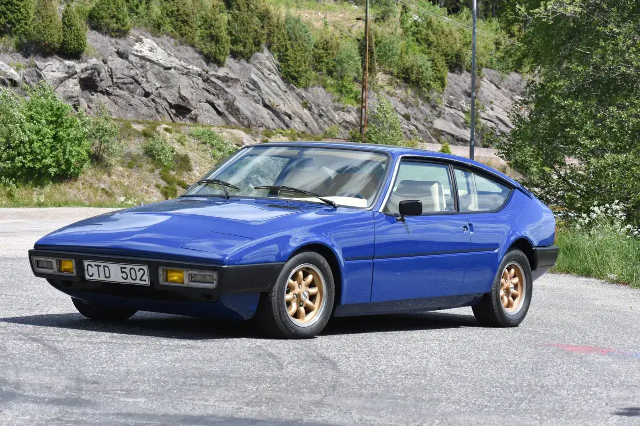 Blå Matra Bagheera sportbil parkerad vid en bergssluttning med grönska.