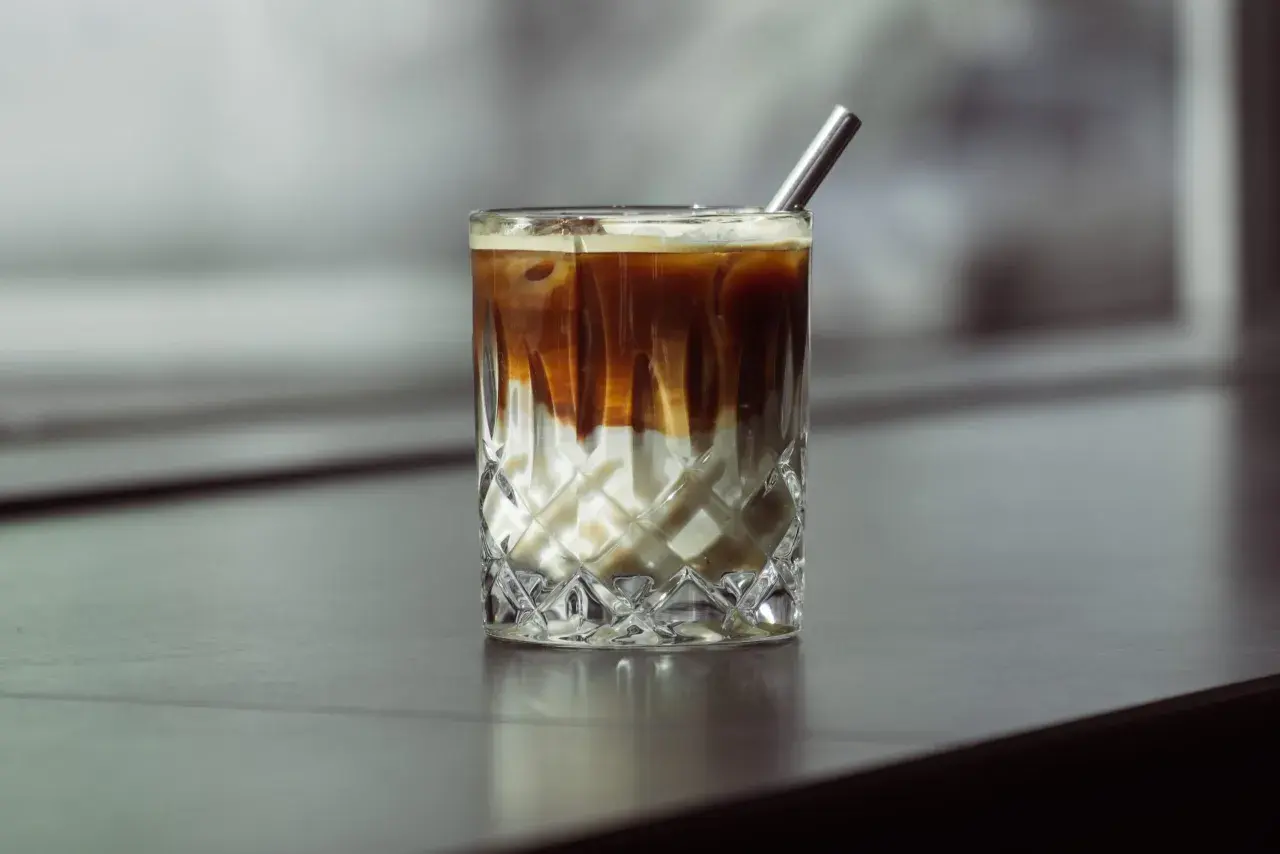 Eiskaffee selber machen ohne Vanilleeis: Ein Glas mit geschichtetem Kaffee und Milch, garniert mit einem Metallstrohhalm.
