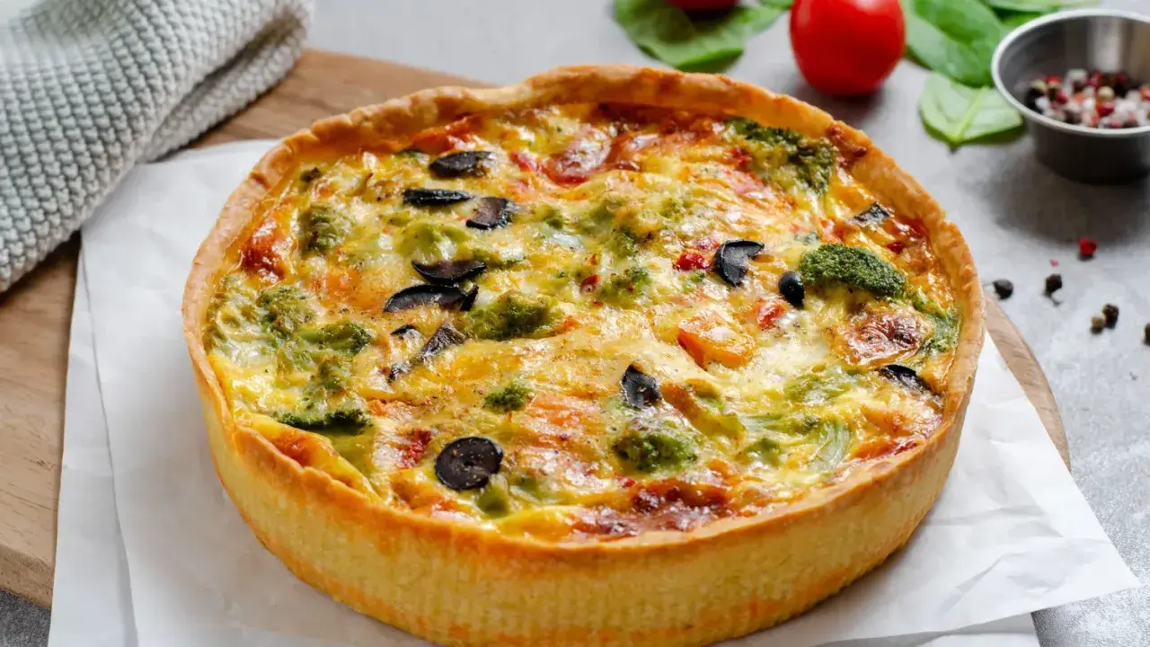 Une délicieuse quiche au poulet, garnie de brocolis, d'olives et de poivrons, prête à être dégustée.