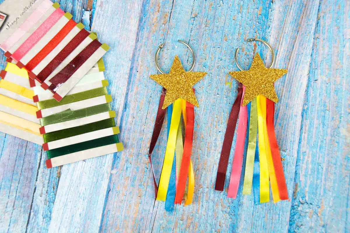 Aretes de carnaval manualidades con estrellas doradas y cintas de colores. Un conjunto de cintas de raso de varios tonos a la izquierda.