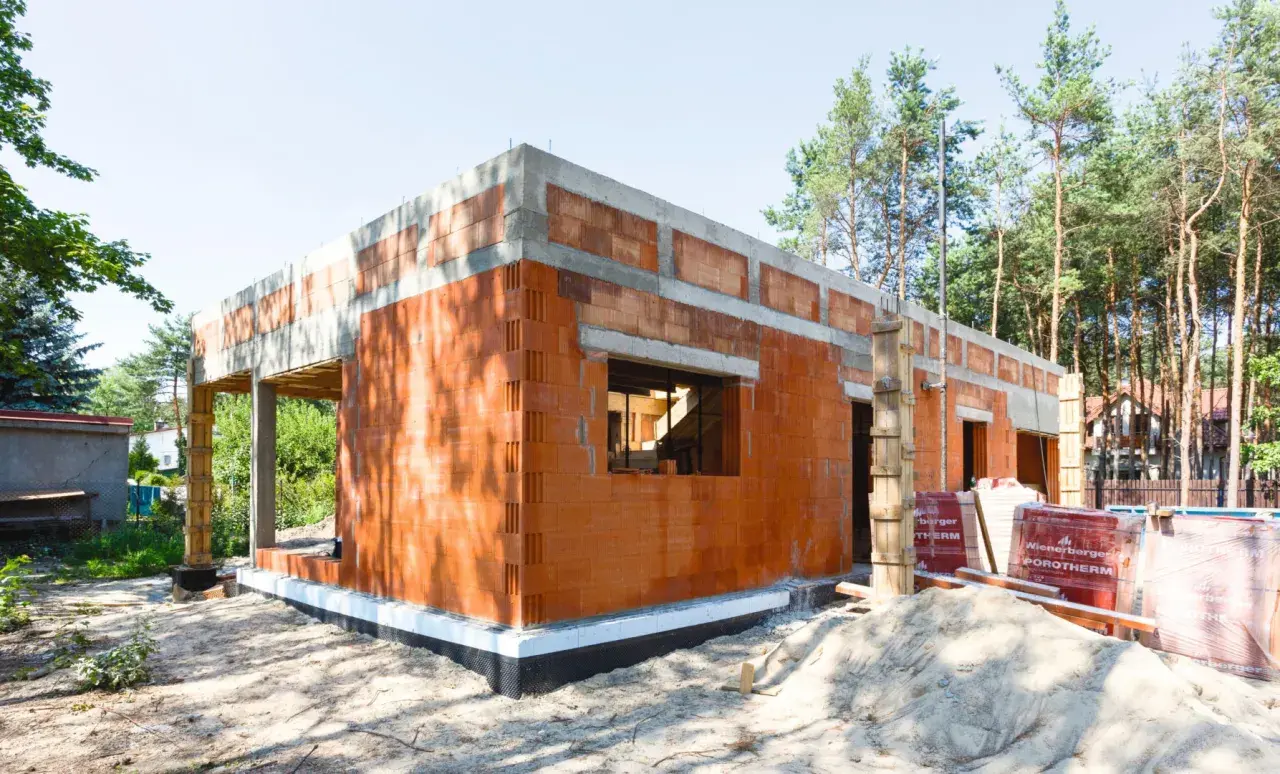 Budowa domu z pustaków ceramicznych. Widać fundamenty, ściany z otworami okiennymi i drzwiowymi. To początek realizacji projektów domów bez pozwolenia.