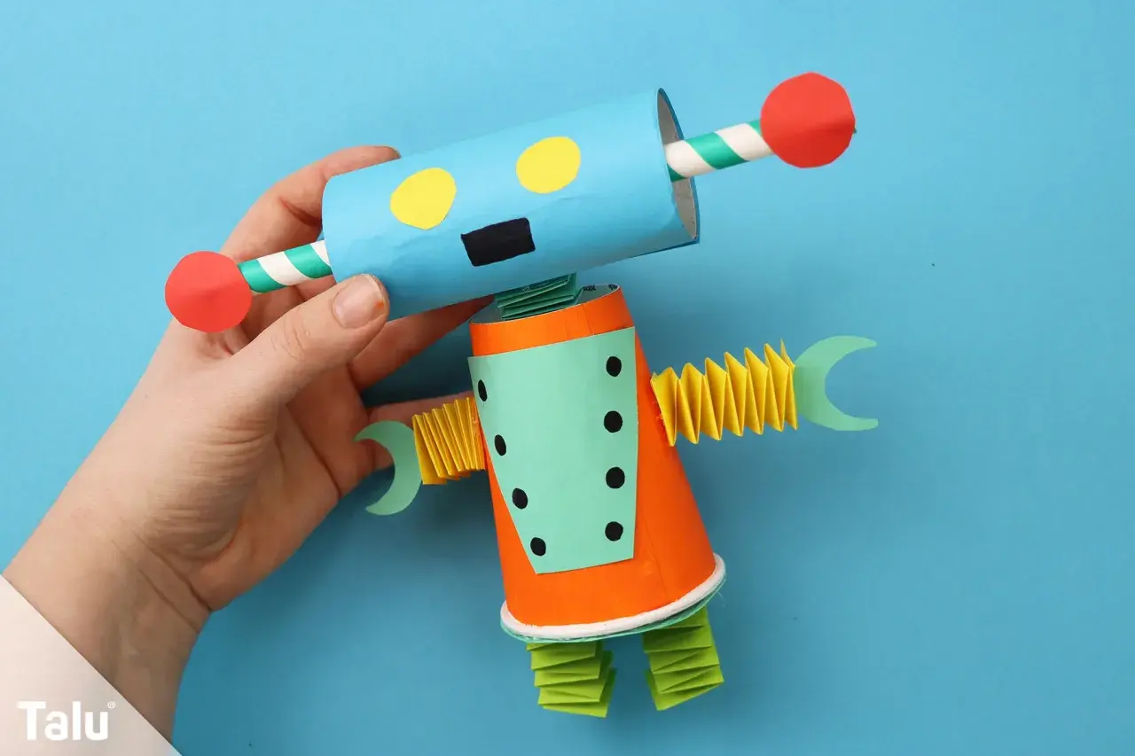 Ein bunter Roboter, der zum **Roboter basteln** einlädt. Er hat einen blauen Kopf mit gelben Augen und einen orangefarbenen Körper.