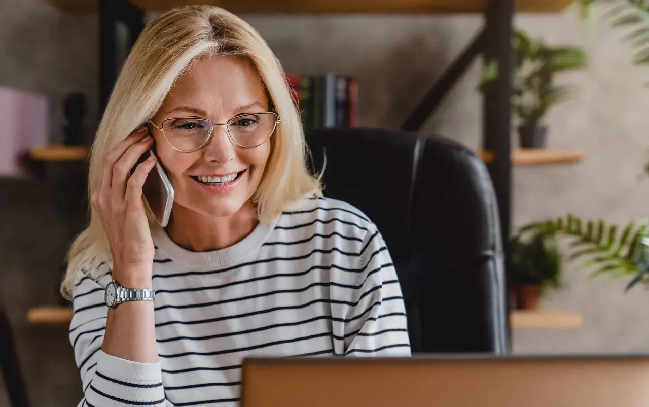 Uśmiechnięta blondynka w okularach rozmawia przez telefon, szukając pożyczki na telefon od zaraz.