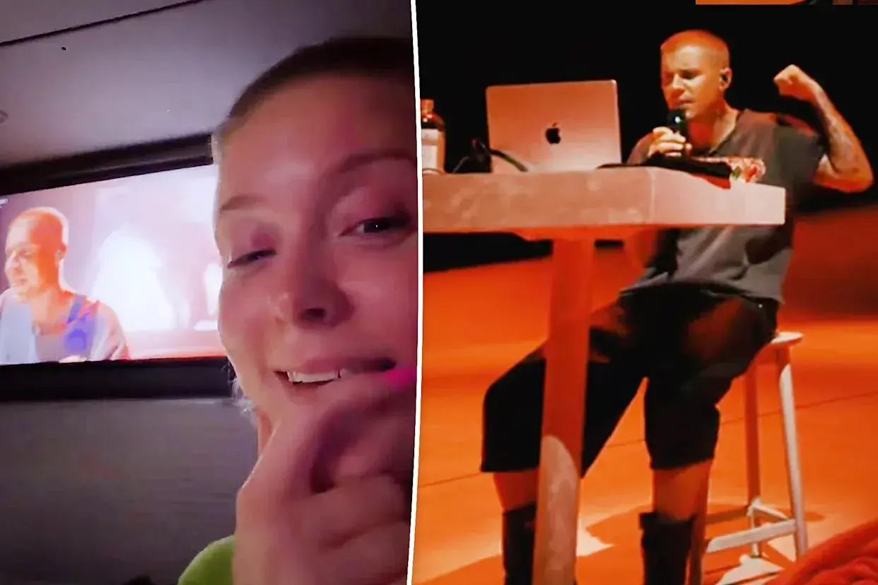 A woman watches a screen showing Justin Parker performing, with a laptop and microphone on a table.