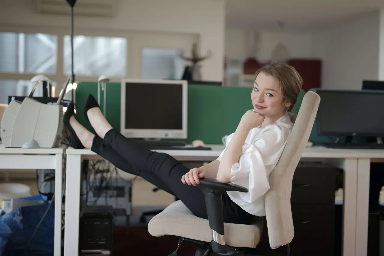 Technik administracji w biurze, z nogami na biurku, odpoczywa po wykonaniu zadań.