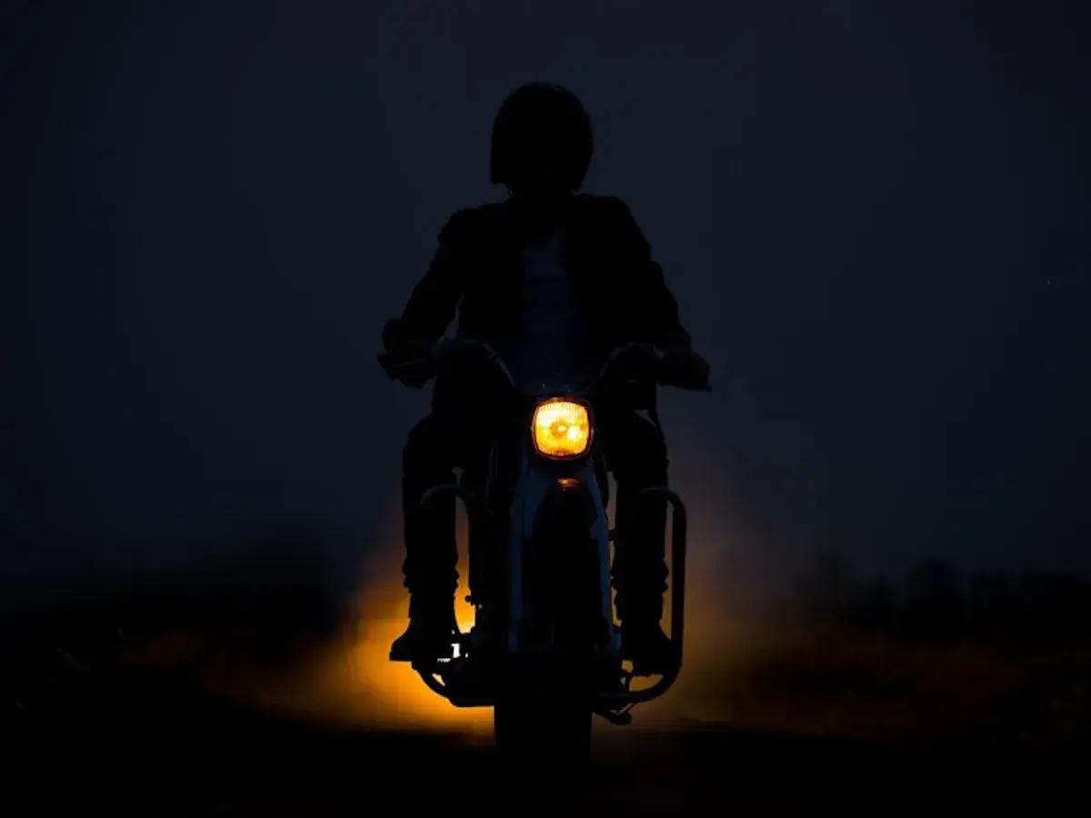 Silhouette d'une personne conduisant une moto dans l'obscurité, le phare jaune illuminant la route. L'aventure de conduire la nuit.