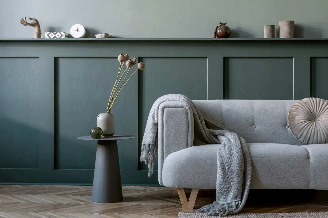 Divano grigio con coperta, vaso con fiori secchi e tavolino su parete con boiserie fai da te.