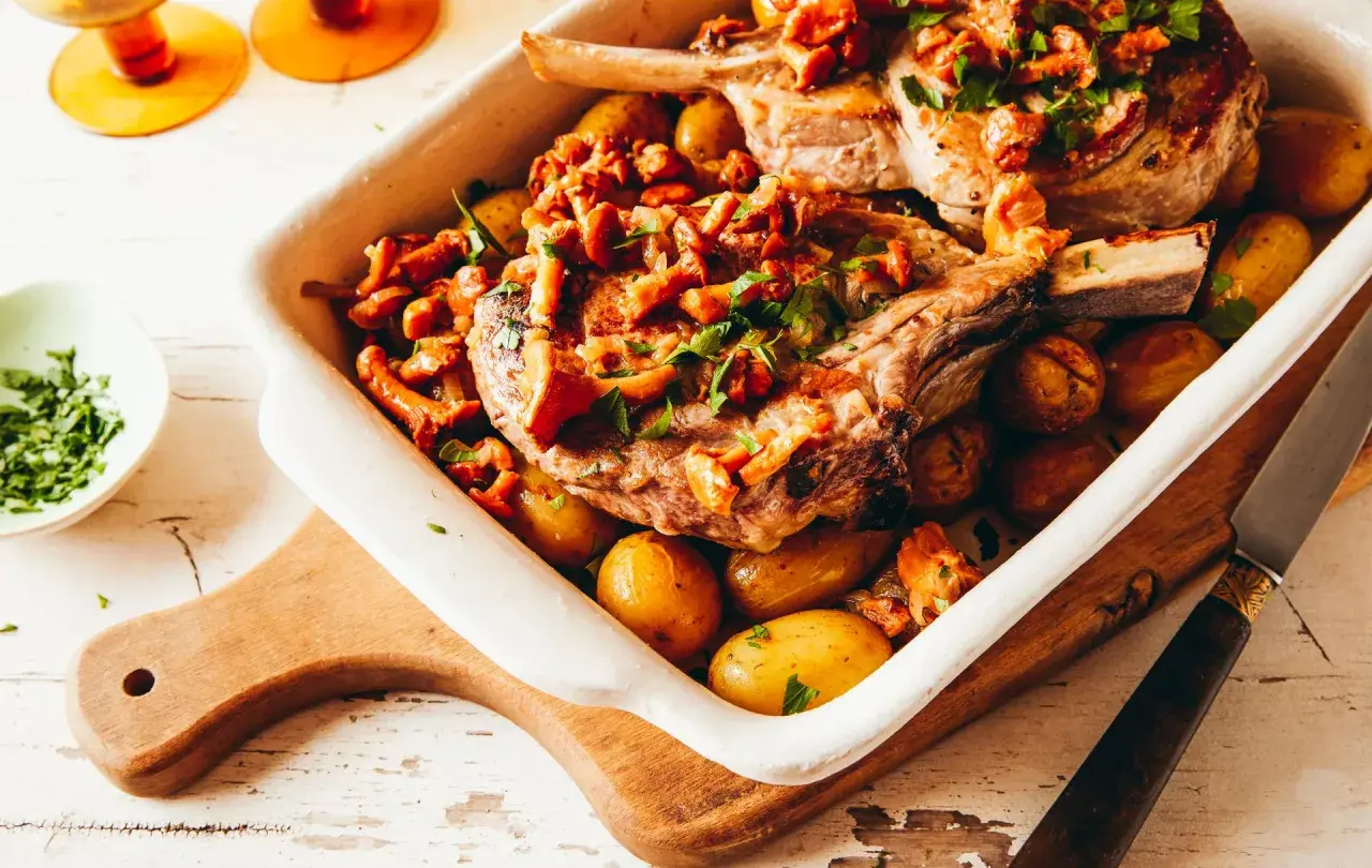 Un plat de viande blanche savoureux, des côtelettes de porc rôties avec des pommes de terre et des girolles, garni de persil frais.