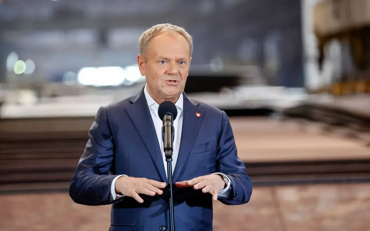 Donald Tusk w garniturze przemawia przy mikrofonie.