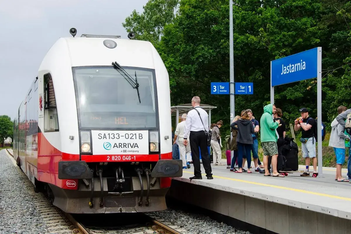 Pociąg Arriva z napisem "HEL" na stacji Jastarnia, gotowy do podróży z Gdańska na Hel. Ludzie czekają na peronie.