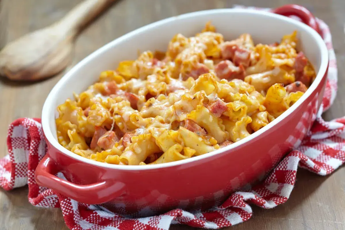 Un plat de gratin de pâtes au jambon, doré et gratiné, servi dans un plat rouge sur une serviette à carreaux.