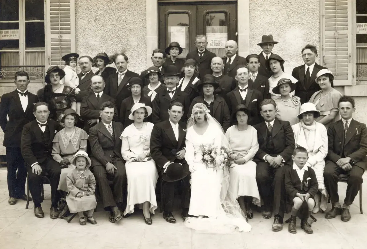 Un groupe de personnes pose pour une photo de mariage. La mariée est au centre, entourée de sa famille et de ses amis. Ce **registre mariage** témoigne d'un jour heureux.
