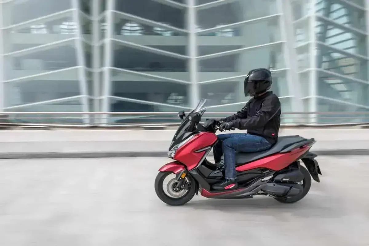 Czerwony skuter z kierowcą w kasku pędzi obok nowoczesnego budynku. To jak tuning 125 na 250, czysta moc!
