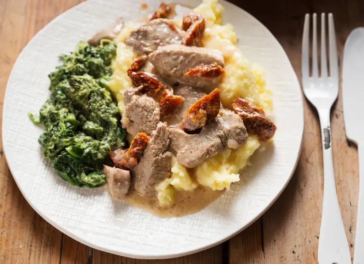 Polędwiczki z suszonymi pomidorami na kremowym purée, obok porcja szpinaku. Pyszny obiad gotowy do podania.